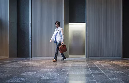 Person walking in a modern corridor with a briefcase.