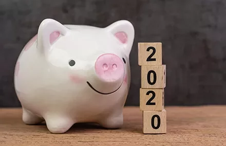 A smiling piggy bank next to wooden blocks stacked to show 2020.