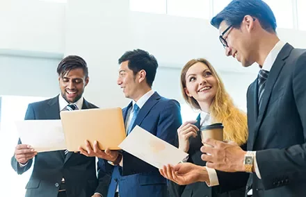 Four business professionals discussing documents and smiling.