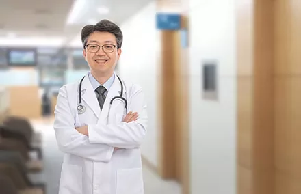 A smiling doctor with crossed arms in a hospital hallway.
