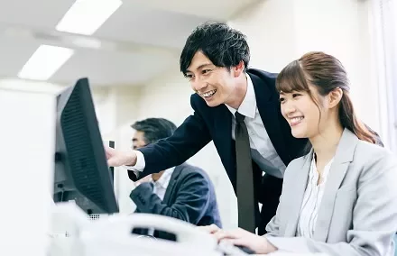 Two colleagues smiling and looking at a computer screen in an office setting.