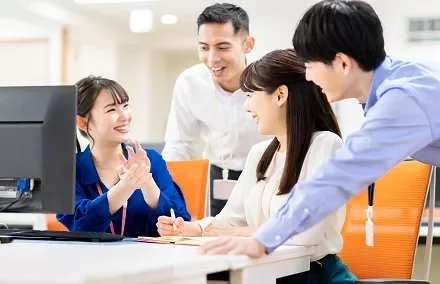 A group of office workers smiling and discussing around a desk.