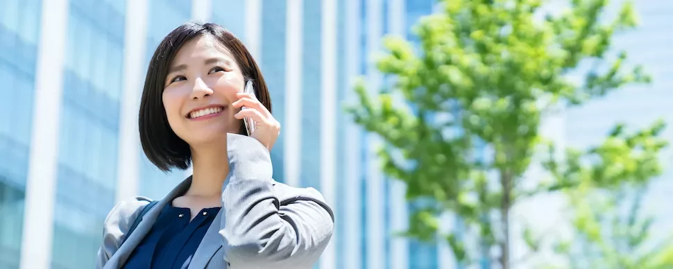 外で電話をしながら微笑む女性、背景にビル。